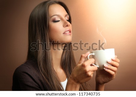 beautiful young woman with cup of coffee on brown background