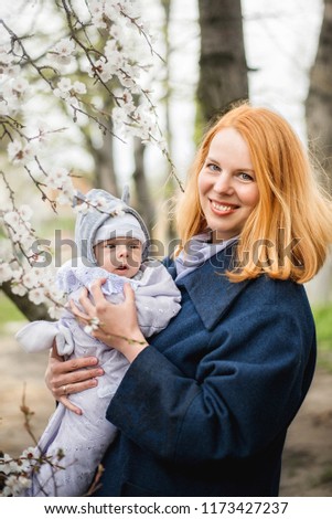 Portrait of a beautiful young woman with red hair, who is holding a newborn baby boy