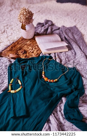 Autumn mood. Dark green dress and yellow jewerly lie on the bed behind a tray with book and flowers