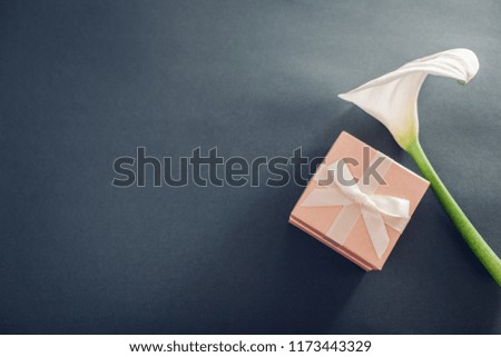 Gift box with white lily. Present with jewellery on grey background. Space