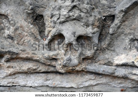 A weathered sandstone relief of a skull with crossbones. A skull with a crown. A hand is reaching for a skull.