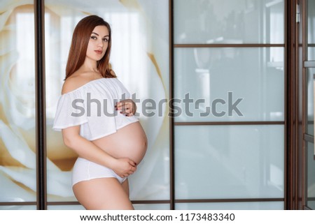 Pregnant Asian woman standing near window at home