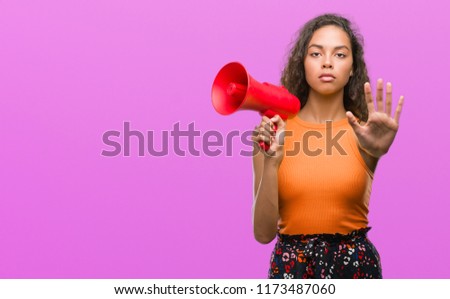 Young hispanic woman holding megaphone with open hand doing stop sign with serious and confident expression, defense gesture