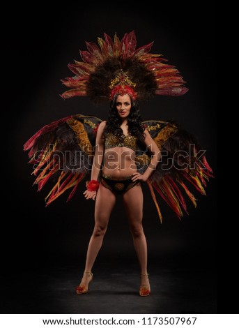Beautiful young woman in bright brazilian carnival costume, decorating with feathers and gems on a black background. Samba dancer.