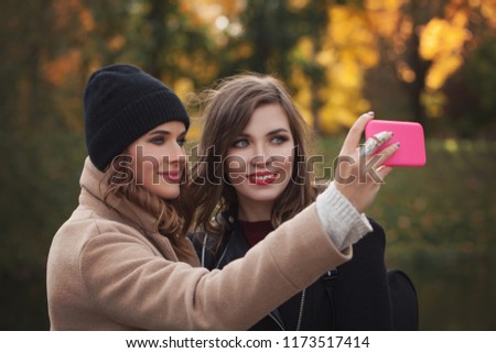 Happy best girlfriends making selfie on smartphone in autumn park outdoors