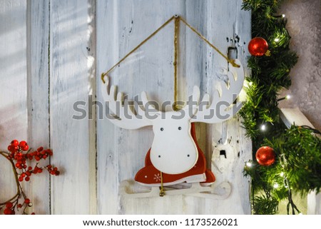 wooden toy moose elk skates in a Santa Claus costume hanging on a wall surrounded by fir branches