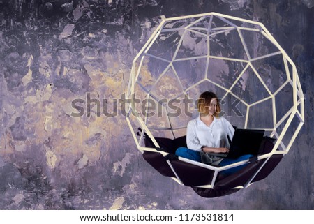 Young modern interior / cloth / fashion designer woman female girl with drawings drafts sketches working in design studio in futuristic structural swing sphere with pillows. 