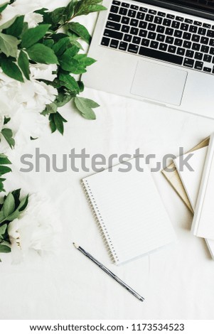 Home office workspace with laptop, notebook, white peonies flowers bouquet on white background. Flat lay, top view.