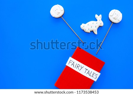 Fairy tales book near candies on blue background top view copy space