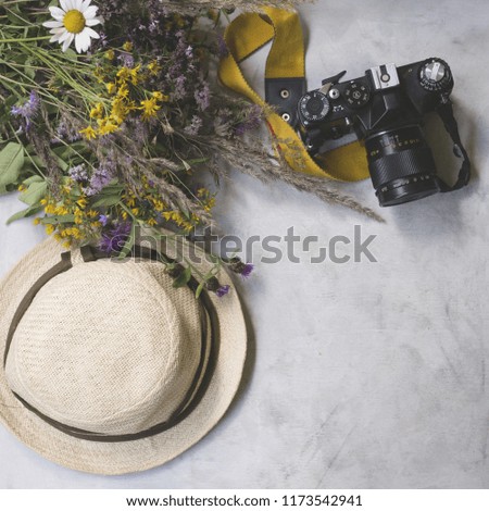 Vintage retro (analog) camera, straw hat with beautiful bouquet of wildflowers on gray background. Holiday  background. Mockup, top view, flat lay, vintage toning