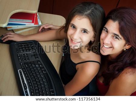 Latin girl and her beautiful mother working on a computer at home ( Image taken from above with the subjects looking at the camera)