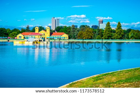 Pond reflections in city park summer time in Denver Colorado USA pine trees grow along waters edge with skyline cityscape in the background water reflections