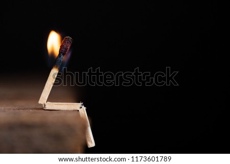 Burning match human sitting on wooden table on a dark background.