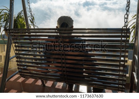 Male tourist sit on swing seeing mountain landscape with low white clouds under brilliant sky. Ideas for travel and feeling.