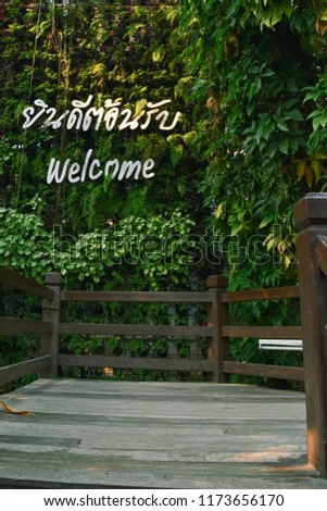 sign on the green leaf background on the wooden stair that was written "Welcome" and Thai translate word of welcome at National park