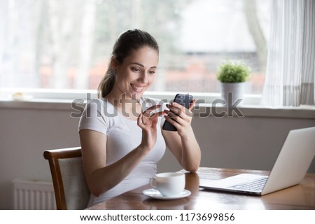 Happy woman working at laptop drinking coffee reading online morning news on smartphone, smiling female get good message from lover or boyfriend, excited girl browsing web or get great offer on mobile Royalty-Free Stock Photo #1173699856