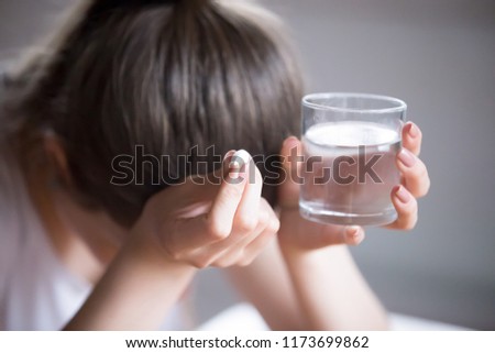 Sick frustrated woman feel unwell holding glass of water and pill doubting to take medicine, exhausted female suffer from migraine or headache ready to have antibiotic or painkiller to ease symptoms Royalty-Free Stock Photo #1173699862
