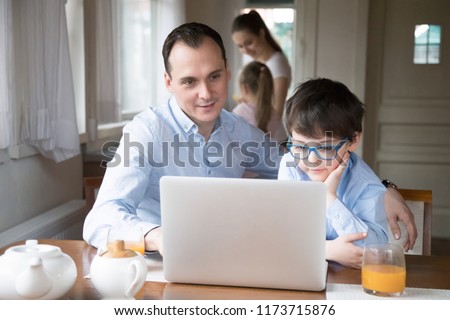 Father and son watching children cartoon online at laptop, dad spending time together with boy teaching him to use computer, curious kid playing game with daddy enjoying morning at home