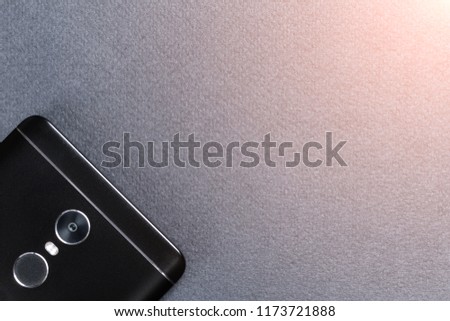 Black smartphone on a black textured surface is the back side. Toned glow.