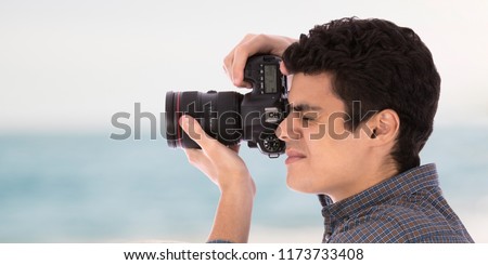 Side shot of the head of young man puts the camera on one eye closed the other one focused taking photos over abstract background.