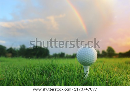 The golf ball is on the orange tee in the golf course, with the rainbow in the background.