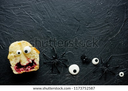 Halloween monster cupcakes decorated with candy eyes on black stone background