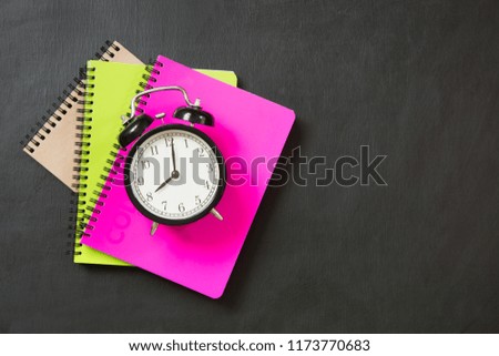 Colorful school supplies and alarm clock on black chalkboard. Top view, flat lay. Back to school.