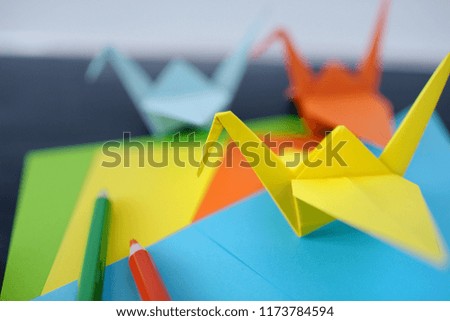 Lesson of origami. Color paper cranes of origami from paper on a black background. Creativity lesson. The kid's hands 