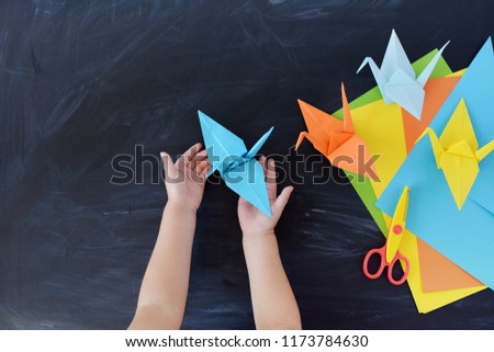 Children's hands do origami from colored paper. Lesson of origami. Color paper cranes on a black background. Creativity. The kid's hands  Royalty-Free Stock Photo #1173784630