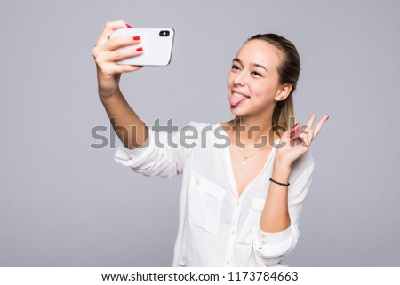 Beautiful woman taking selfie and showing victory sign with perfect smile isolated over gray