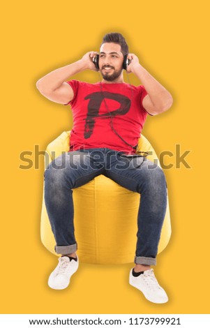 Young man sitting on yellow beanbag look away listens to music happily, over yellow background.