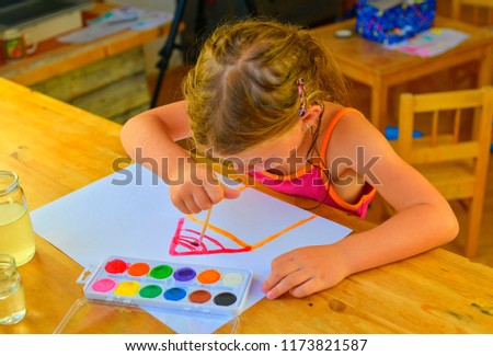 Little girl painting simple picture. Cute girl painting with watercolors. 