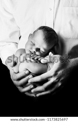 Newborn baby, lying on his father's hand. Studio shoot, on black background. Beautiful male hands. Father's care. Newborn shooting. Portrait. Skin to skin
