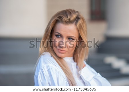 pensive young blond woman on building background with columns. sad girl in a white blouse