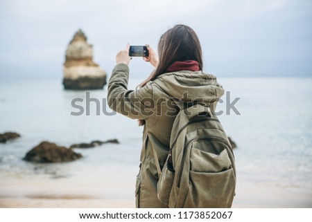 Girl tourist with a backpack photographing a beautiful landscape standing on the Atlantic coast.