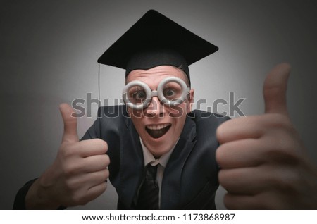 Graduate student in the cap is showing a thumbs up isolated on gray background. Education concept.