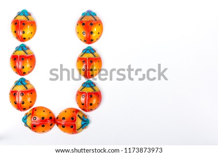 Flat lay with the letter U formed by a group of ceramic ladybugs with red, orange, yellow, blue and black colors on a white background with space for text
