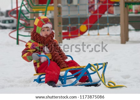 Cute little child in winter cloth on sledge on snow-covered kids playground.