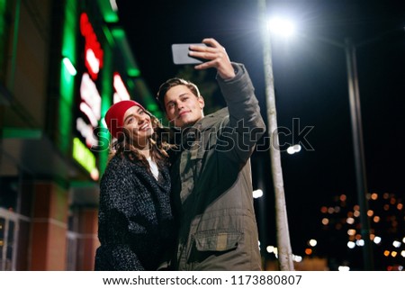 Couple Taking Photos On Phone On Street In Evening. Fashionable Young People Making Selfie Outdoors. High Resolution