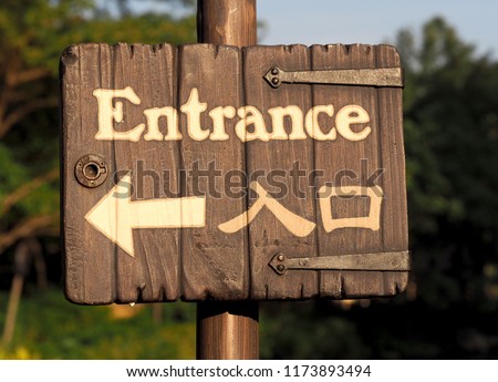 Bilingual wooden entrance signs with a white arrow to the left