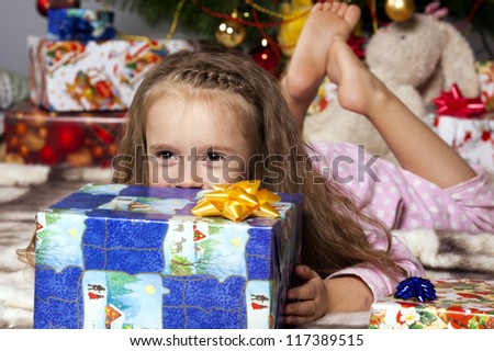 Girl in pajamas lying under the Christmas tree with gift in hand