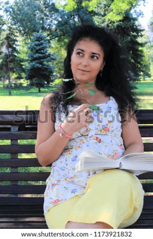 A young beautiful woman with long curly hair is reading a book in the park