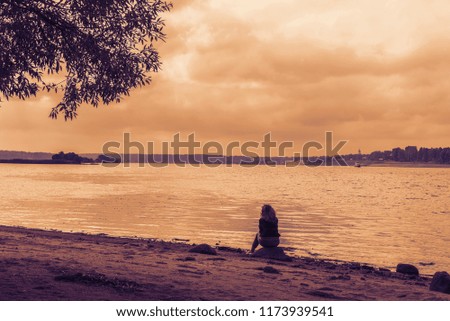 A girl sits on the river bank. Toned