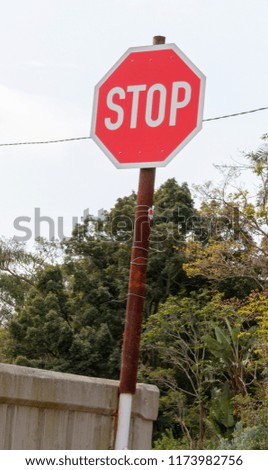 A front view of a red and white stop sign attached to a rusted thin pole on the side of a bridge 