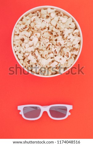 3d glasses and a paper cup with popcorn are isolated on a red background, a view from above.Flat lay. Cinema Concept