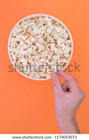 Male hand takes a popcorn from a paper cup on a orange background. Man eats popcorn. Isolated. Cinema Concept. Flat lay. Copyspace.