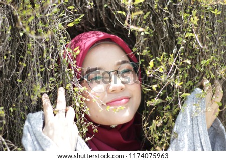 cute young girl wearing hijab by the park and close to greenery leaf