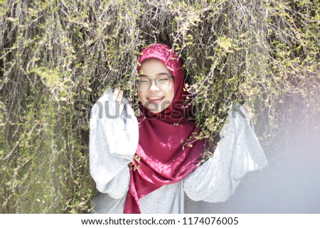 cute young girl wearing hijab by the park and close to greenery leaf