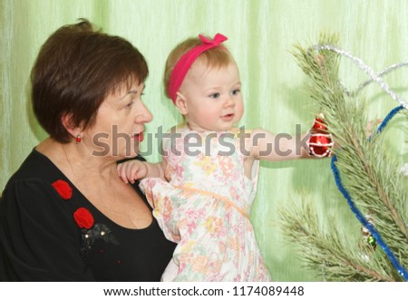 Grandmother with her granddaughter on their hands looking at the toys on the New Year tree.