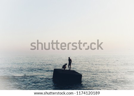 Silhouette girl and boy on big alone stone in sea. Free place for text, white corners and sky. Woman and man, two people evening silhouettes. 